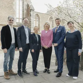 Drei Frauen und drei Männer blicken freundlich in die Kamera. Sie stehen vor einem Gebäude, das mal eine Kirche war und jetzt eine Ruine ist.